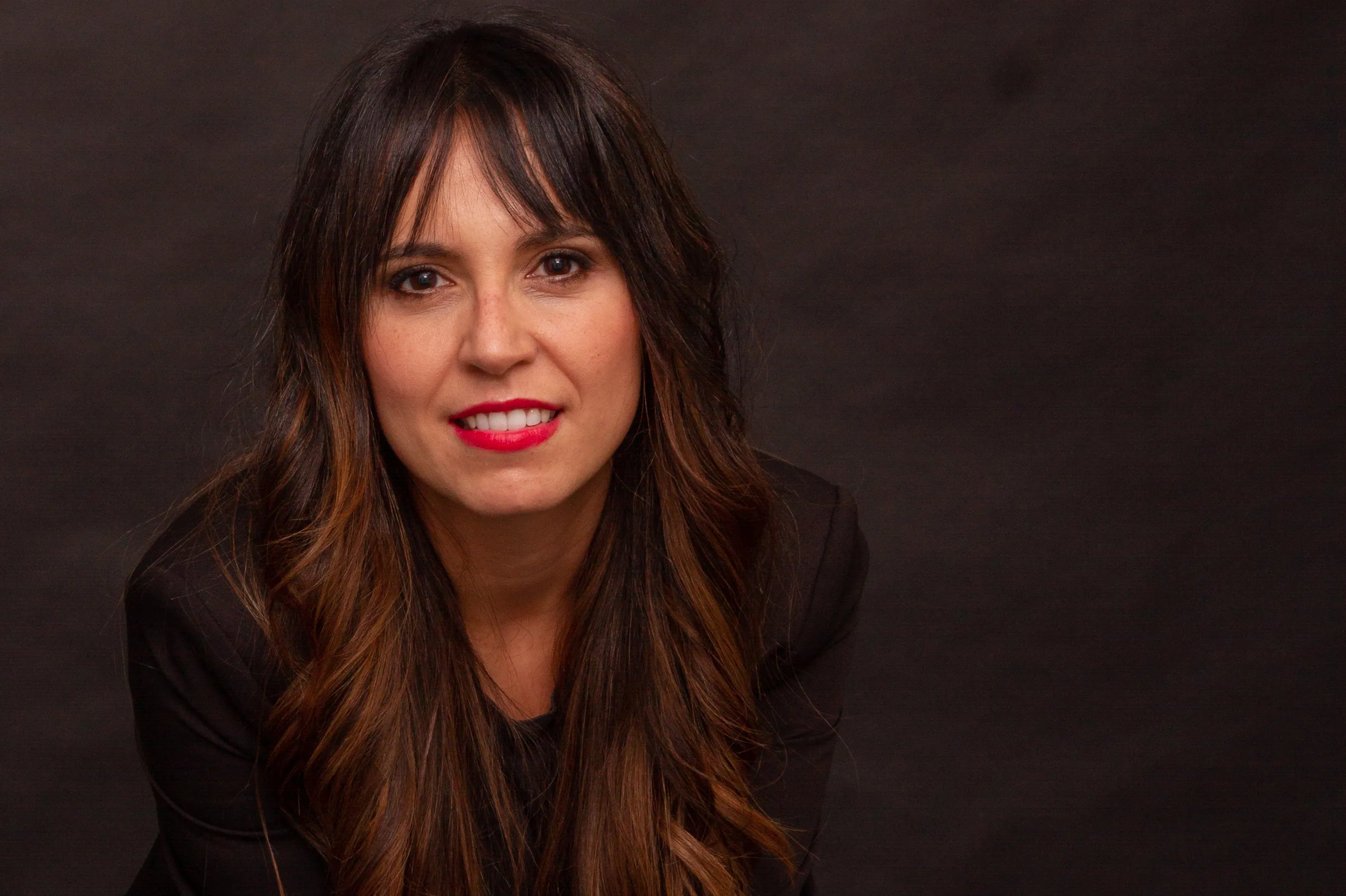Almudena Lebrero sonriendo, retrato sobre fondo oscuro