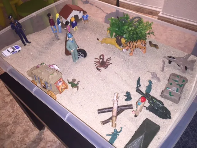 Caja de arena con figuras de personas, animales, vehículos y soldados colocadas por un niño