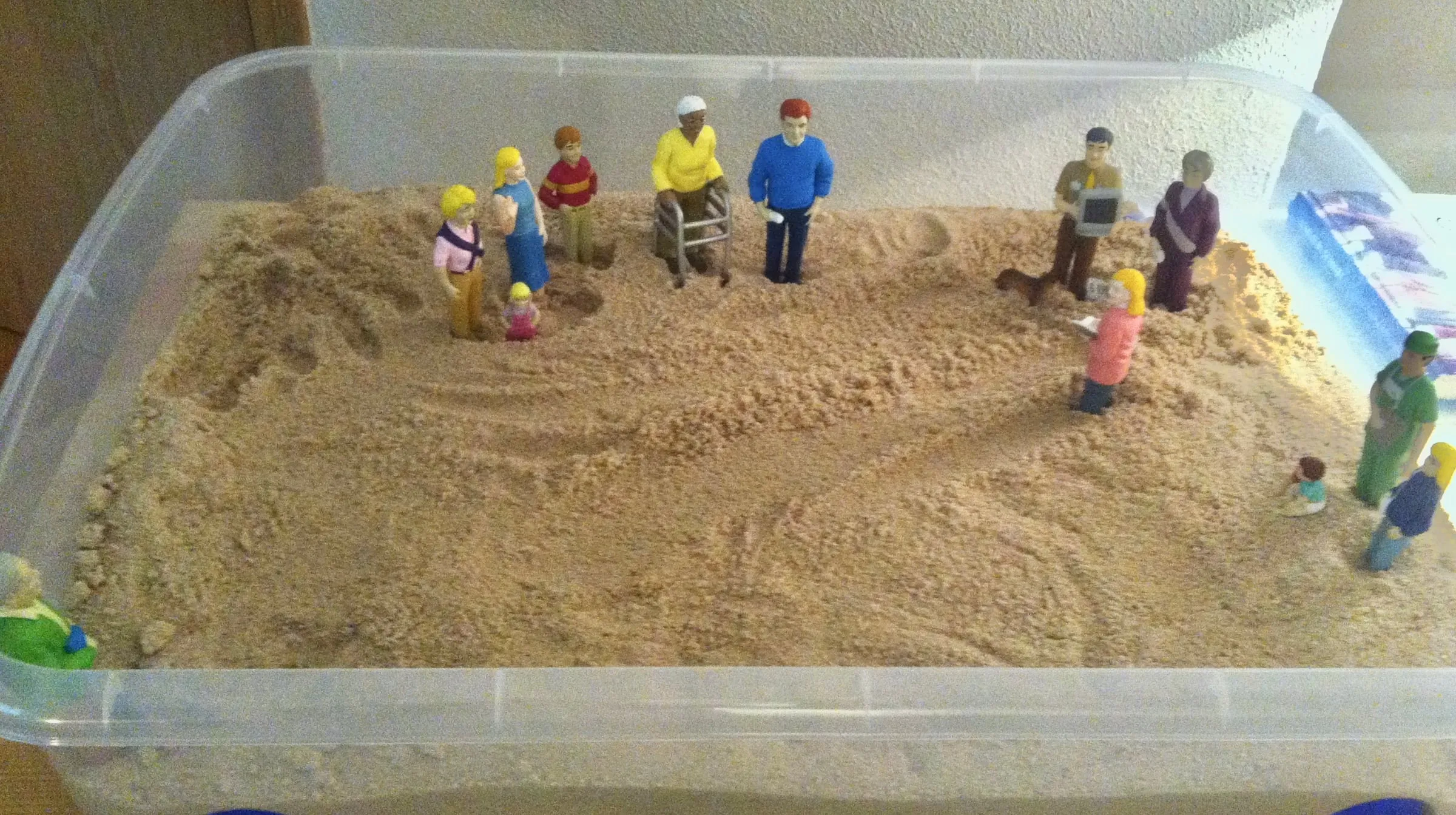Caja de arena con figuras de personas de distintas edades colocadas sobre la arena